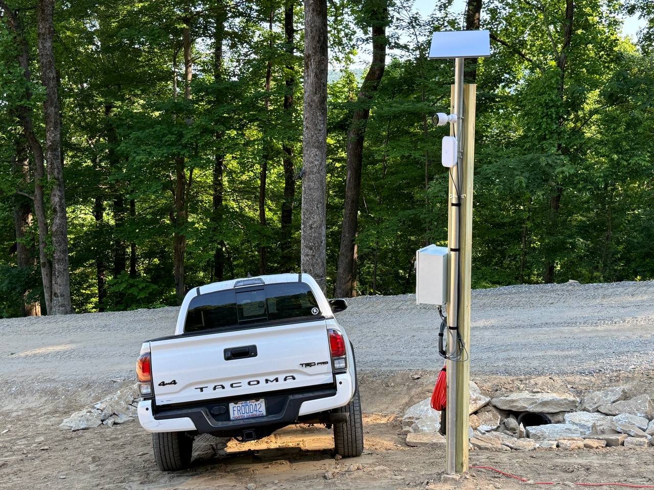 Temporary construction site connectivity and surveillance system mounted on a post beside a gravel access road